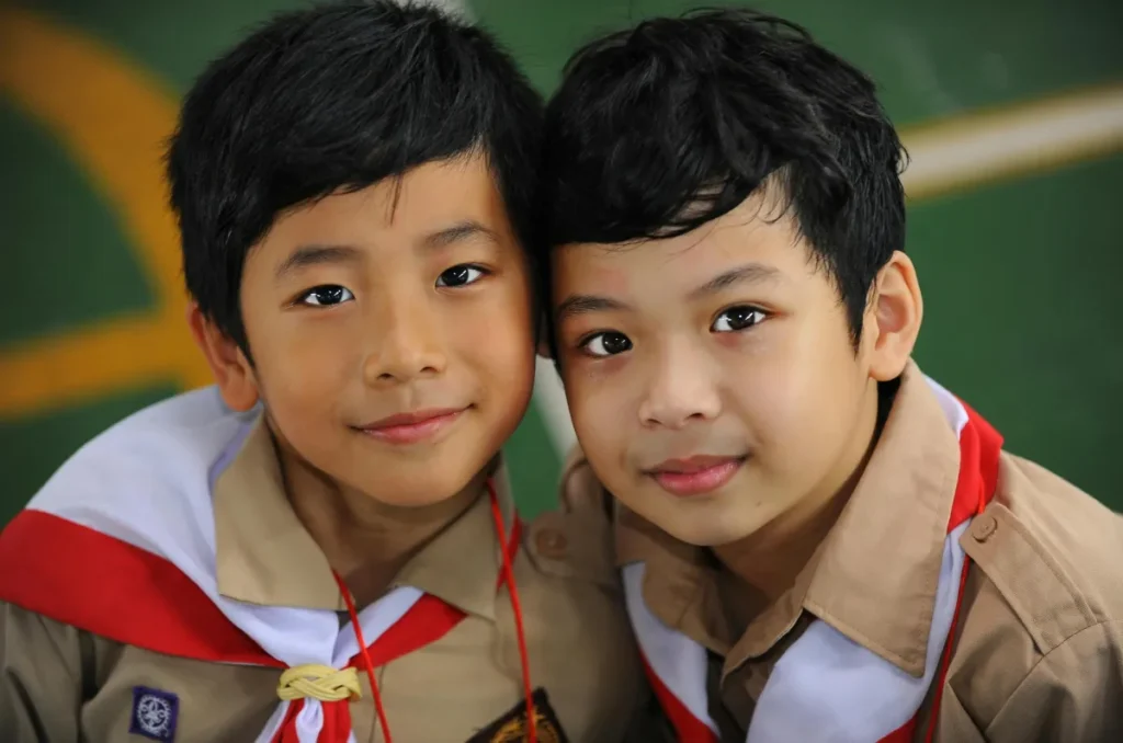 Dua anak laki-laki Indonesia tersenyum mengenakan seragam pramuka coklat di Jakarta